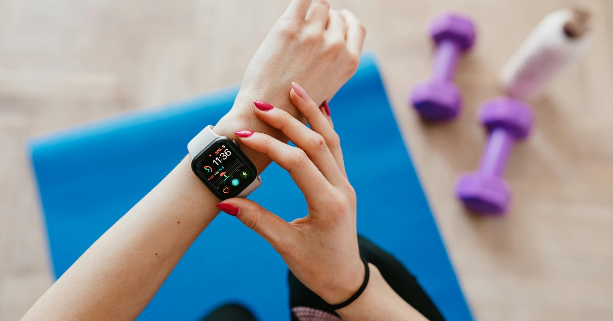 Person adjusting smartwatch during workout beside yoga mat and dumbbells